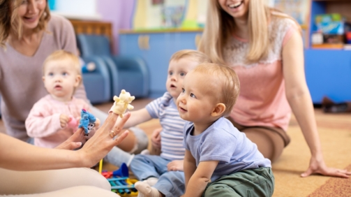 Nursery teacher and babies playing with educational toys in kindergarten or day care centre
