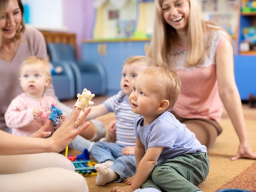 Nursery teacher and babies playing with educational toys in kindergarten or day care centre